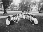Sixteen young women wearing uniforms sit on the lawn of the college grounds.