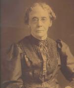 Sepia photgraph of an elderly lady. She is wearing a dress with a ruffled front and spectacles.'