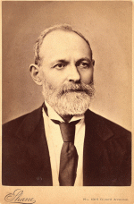 Sepia photgraph, head and shoulders of a bearded man, wearing a suit, white shirt, and tie.