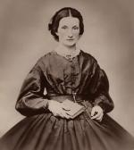 Image of a young woman wearing a full skirted dress with a lace collar, and she is holding a book.