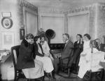 A small group of people, sitting in chairs and wearing headphones, are listening to a radio broadcast.