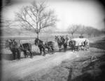 Six mules are hitched to the Lime Wagon. A farmer sits atop the rear left mule's back and another stands to the side of the wagon. 