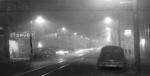 Streetlights pierce a dense fog that is so thick, it looks like nightfall on a city street.